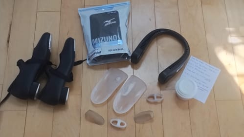 Specialized footgear, black tap shoes, a neck-cooling device, and a paper list of classes are arranged on a wood floor.