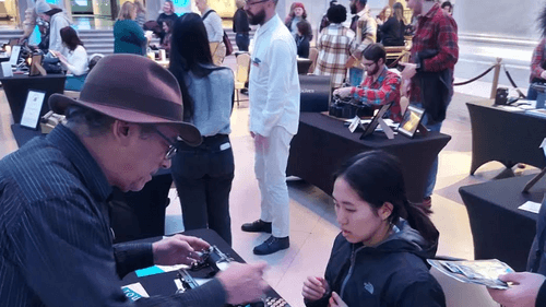 In a large room of exhibitors at small black tables, Kravitz shows a young girl how to use a typewriter.