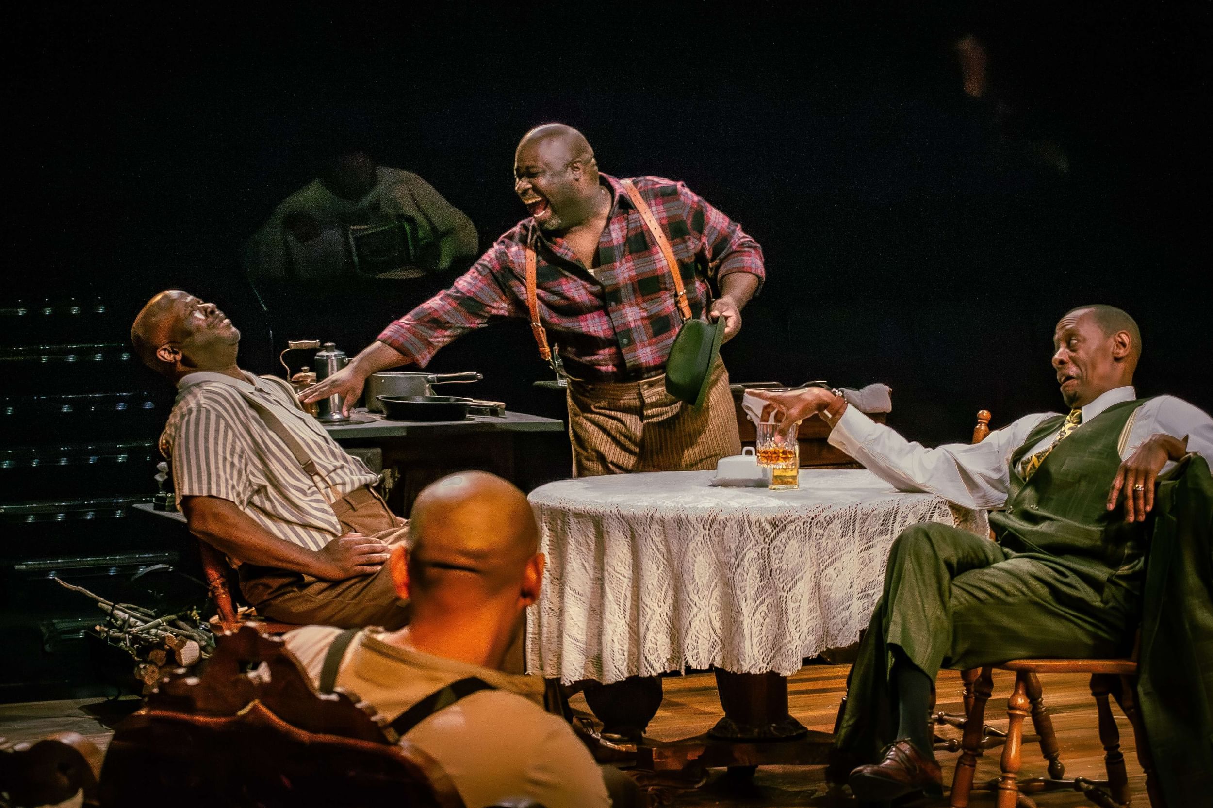 Three Black men in 1930s garb carouse around a small round table with a white lace cloth.