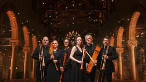 6 Performers in all black formalwear, holding various wind and string instruments, pose in hall with tall, wide arches