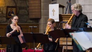 On a chancel, the three black-clad musicians play wooden recorders ranging from about one foot to three feet long.