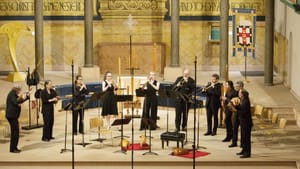 10 Piffaro musicians, all wearing black, perform in a semicircle on a bright Christian chancel turned into a stage.