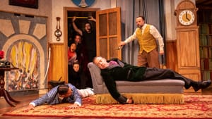 The ensemble onstage: two miming death (one on a couch, one on the floor), and four shocked crew members crowding in a door.