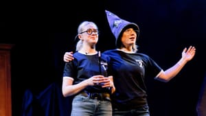 Gann and Bell on stage, in casual top and jeans. Dumbledore wears a wizard's hat.