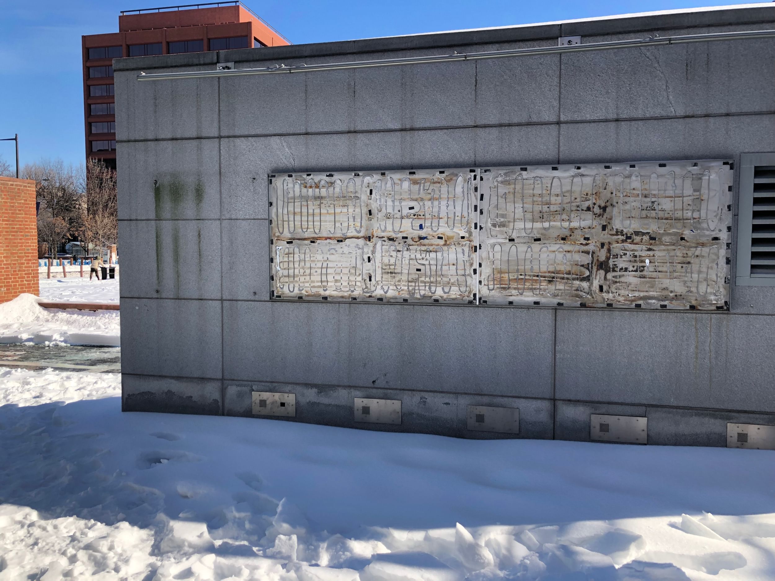 Cement wall with a messy metal rectangle where historical signage about slavery used to be.