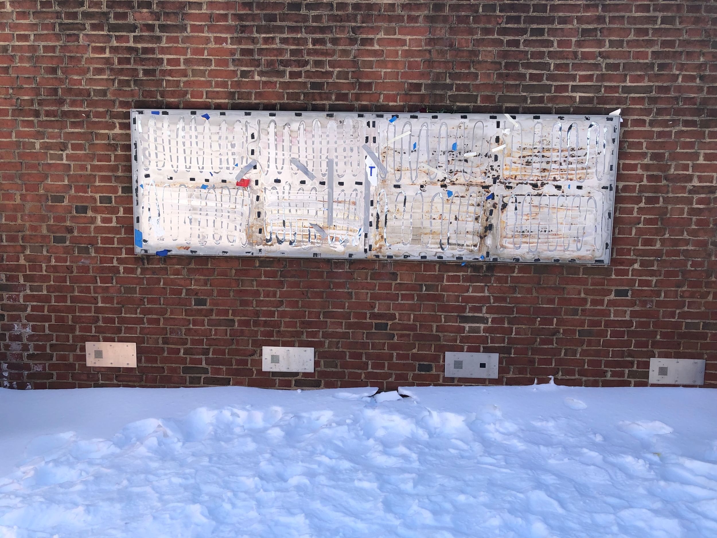Brick wall with a messy metal rectangle where historic signage on slavery used to be. There is snow on the ground below.