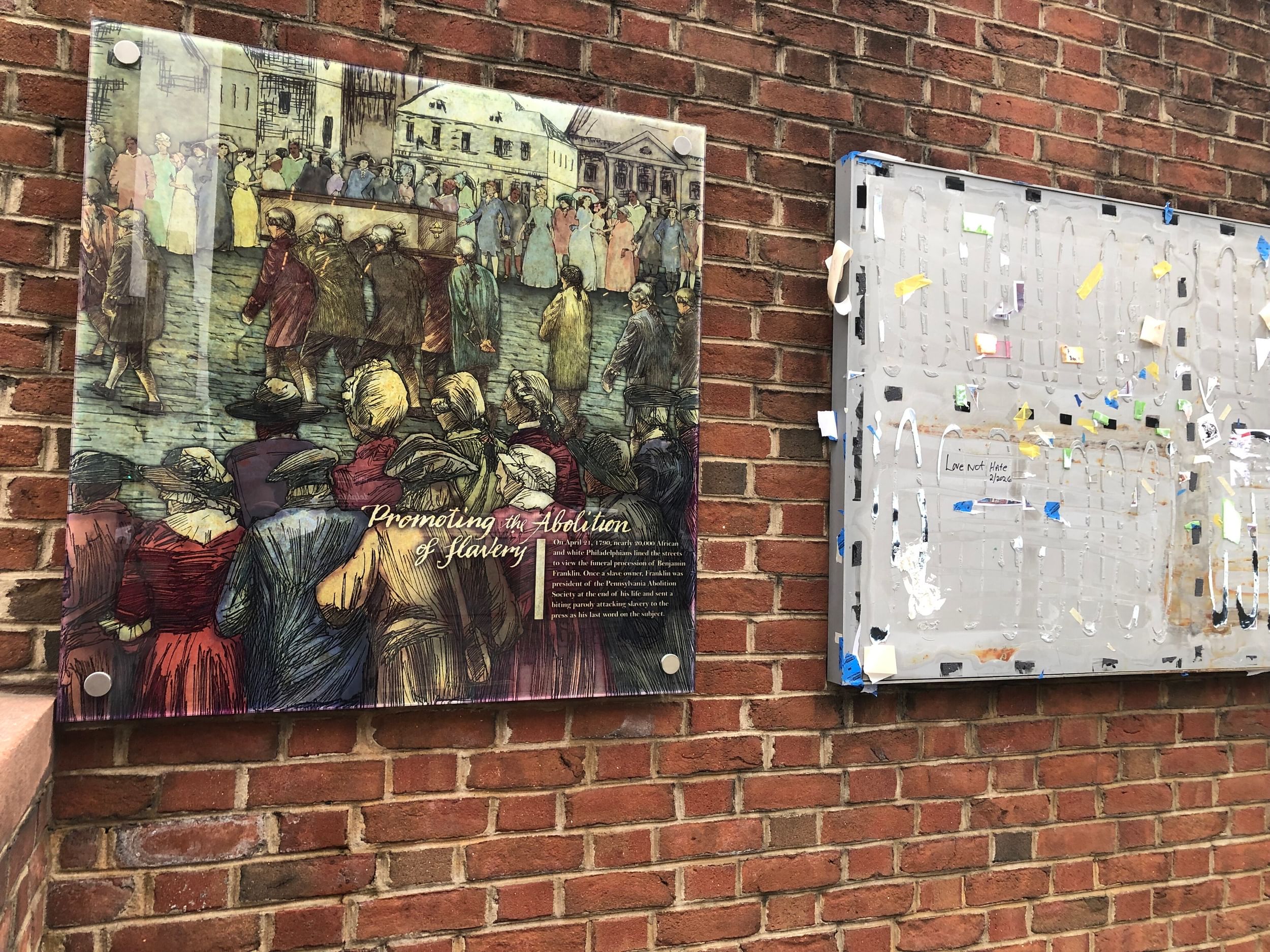 A glass panel with an etching of integrated 18th-century Philadelphians at a funeral procession next to a panel ripped away.