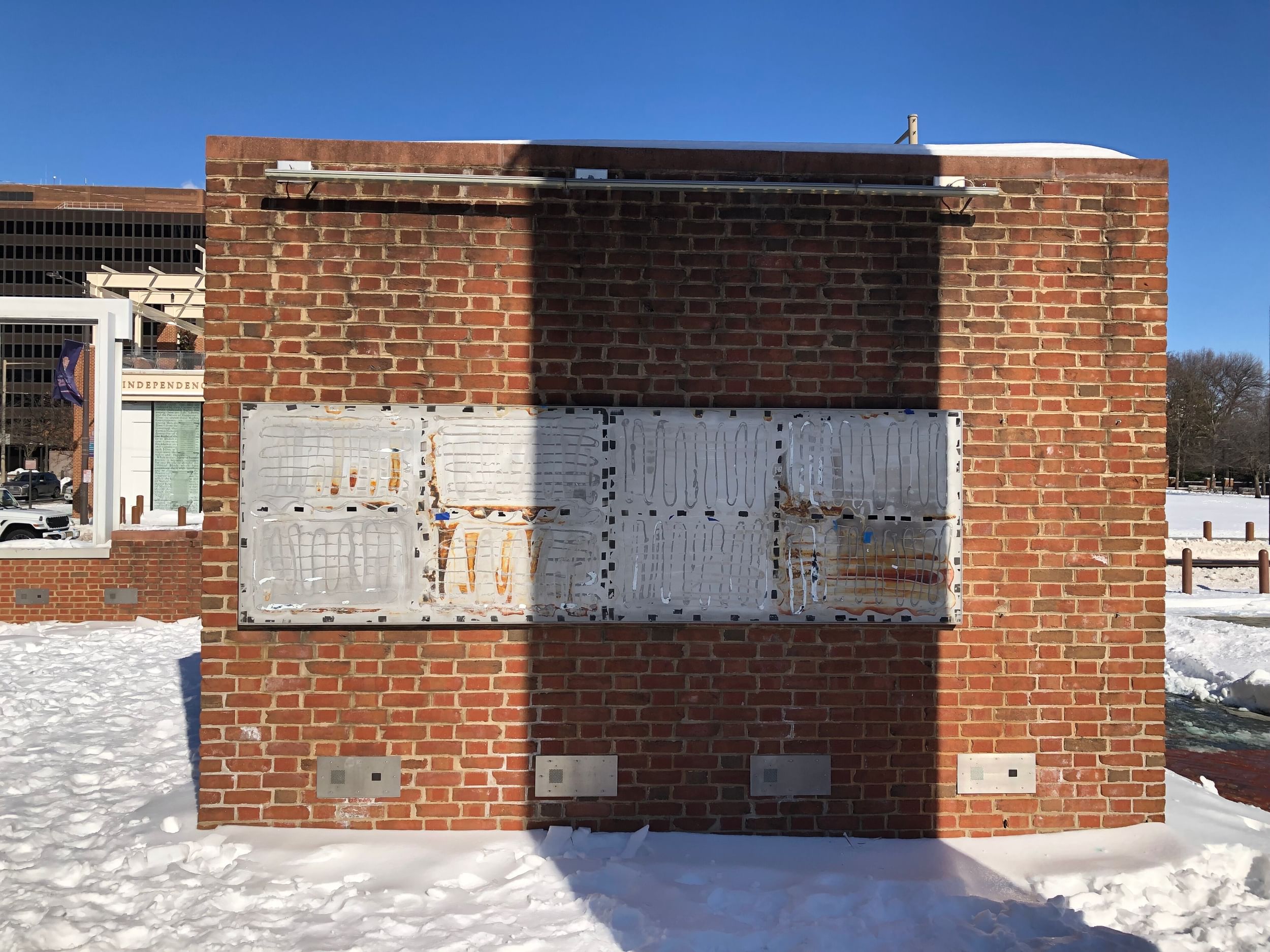 An outdoor brick wall with a messy metal rectangle where signage used to be. The sky is blue and snow is on the ground.