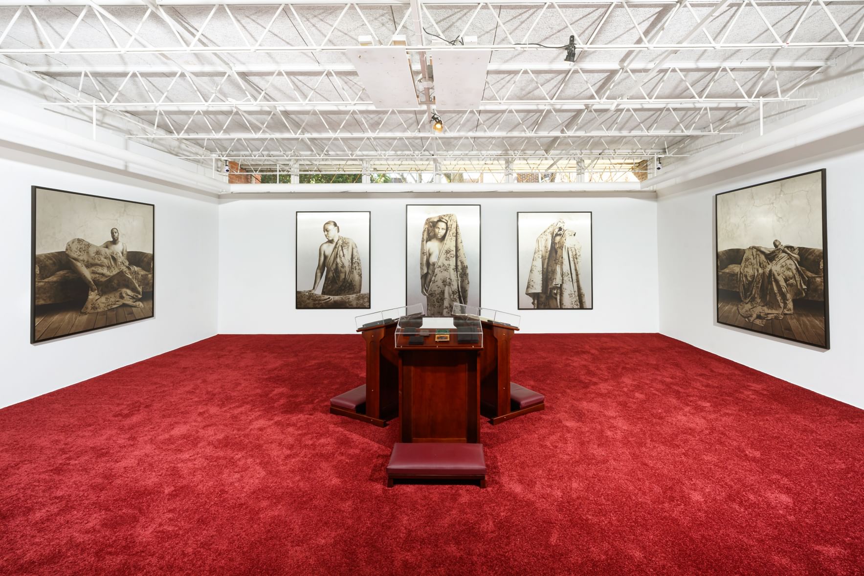 Spacious white-walled gallery with red carpet has large sepia daguerreotypes of Baxter, with four prie-dieu at the center.