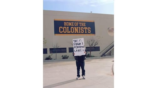 Camargo’s face is hidden by the sign he’s holding, reading “This is Tongva & Acjachemen Land!!”, next to a high school