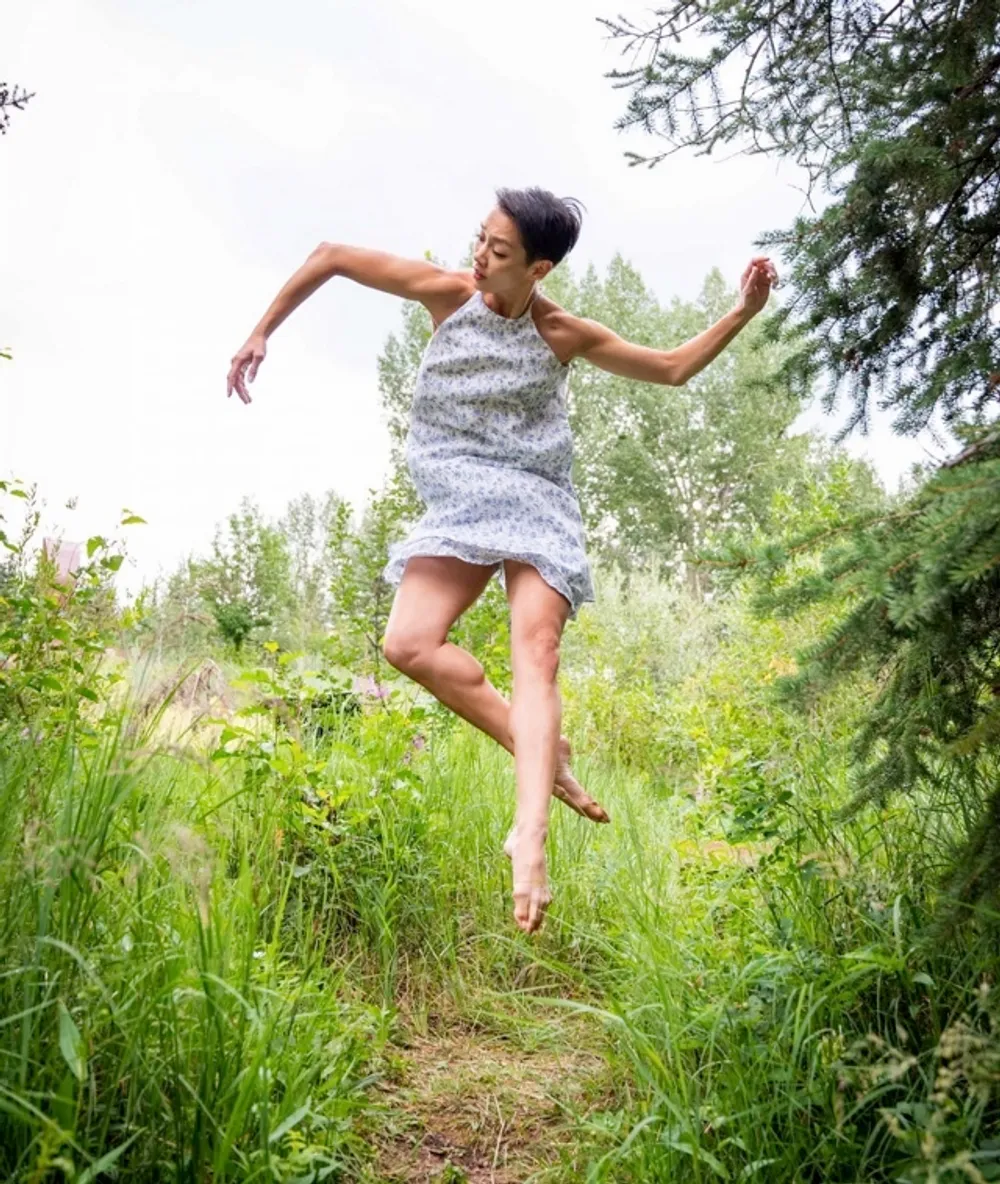 Caili Quan in mid movement as she is captured midair, outdoors in a grassy area with many trees.