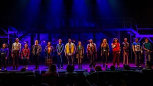 14 actors, in evocative 90s clothes, pose in a line onstage, bathed in blue and purple light.