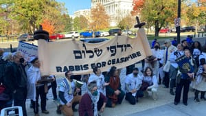 Near the US Capitol, a crowd, many wearing yarmulkes & tallits, hold a giant Torah-style scroll saying Rabbis for Ceasefire.