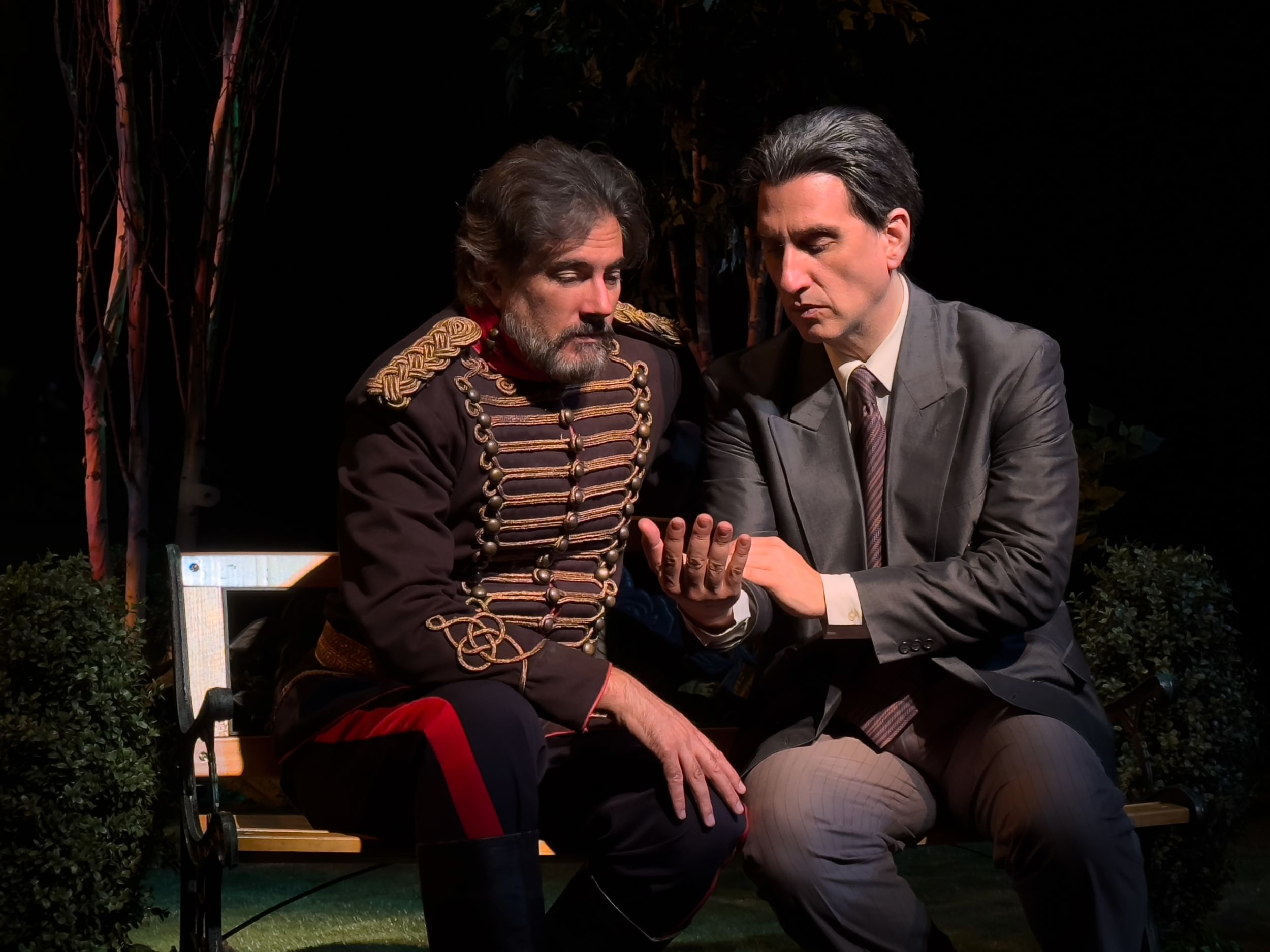 Silvestri, in ornate turn-of-the-century military jacket, sits with Felder, in a gray suit. They examine Felder’s right hand