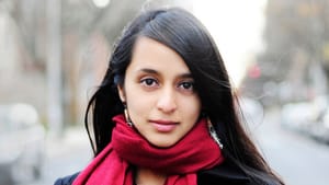 Portrait shot of Esmail, an Indian American woman. She wears a black coat and red scarf against an outdoor city backdrop.