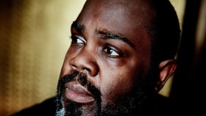 Close-up portrait shot of Mobley, a Black man with a full beard, dark with some light gray, looks on towards left of frame