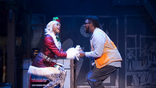 Javon King, in zebra tights and Santa dress, and Shafiq Hicks, in an orange vest & baggy jeans, hold hands and sing joyfully