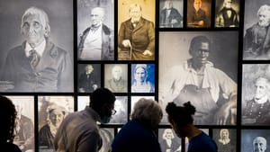 A group looks on at a wall panel featuring old portraits of historical figures, many in black and white or sepia tone