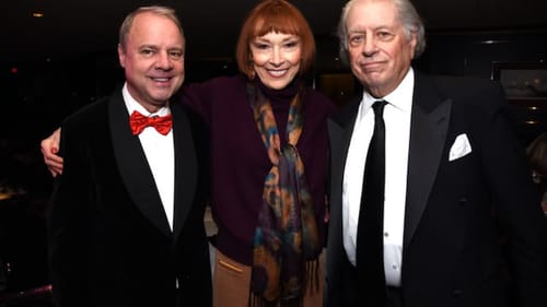 The two men in black tie stand with Akers in the middle, her arms around them. They’re all smiling.