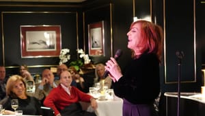 McArdle, a 61-year-old white woman with red hair, sings smiling into a mic in a fine-dining restaurant.