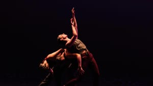 Three dancers tangled in movement on stage, with one dancer leaning back on backs of other dancers and looking up