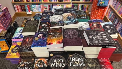 A large display of thick, fancy-looking romantasy paperbacks stacked on bookstore table.