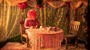 A tea party in an ornately draped tent of lace, with one guest who has a giant pink rose instead of a face.