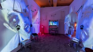 A large dressing room installation with white walls washed in blue light and huge projections of Jarboe’s face.