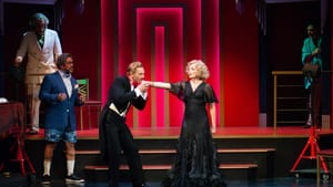 At center, Matarrese, in a tux, bends to kiss Heflin’s outstretched hand. She wears a black ball gown and looks worried.