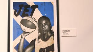 Black & white image of Dawn Stanley holding up a basketball, with a serious expression, on geometric blue & white background