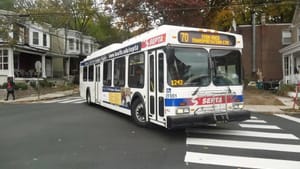 A route 70 SEPTA bus turns a corner in a Philly neighborhood with autumn trees.