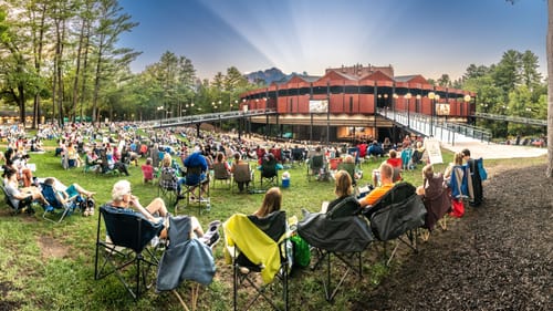 Outdoor view of the SPAC amphitheater, with hundreds of outdoor concert-goers sitting in lawn chairs on the surrounding grass