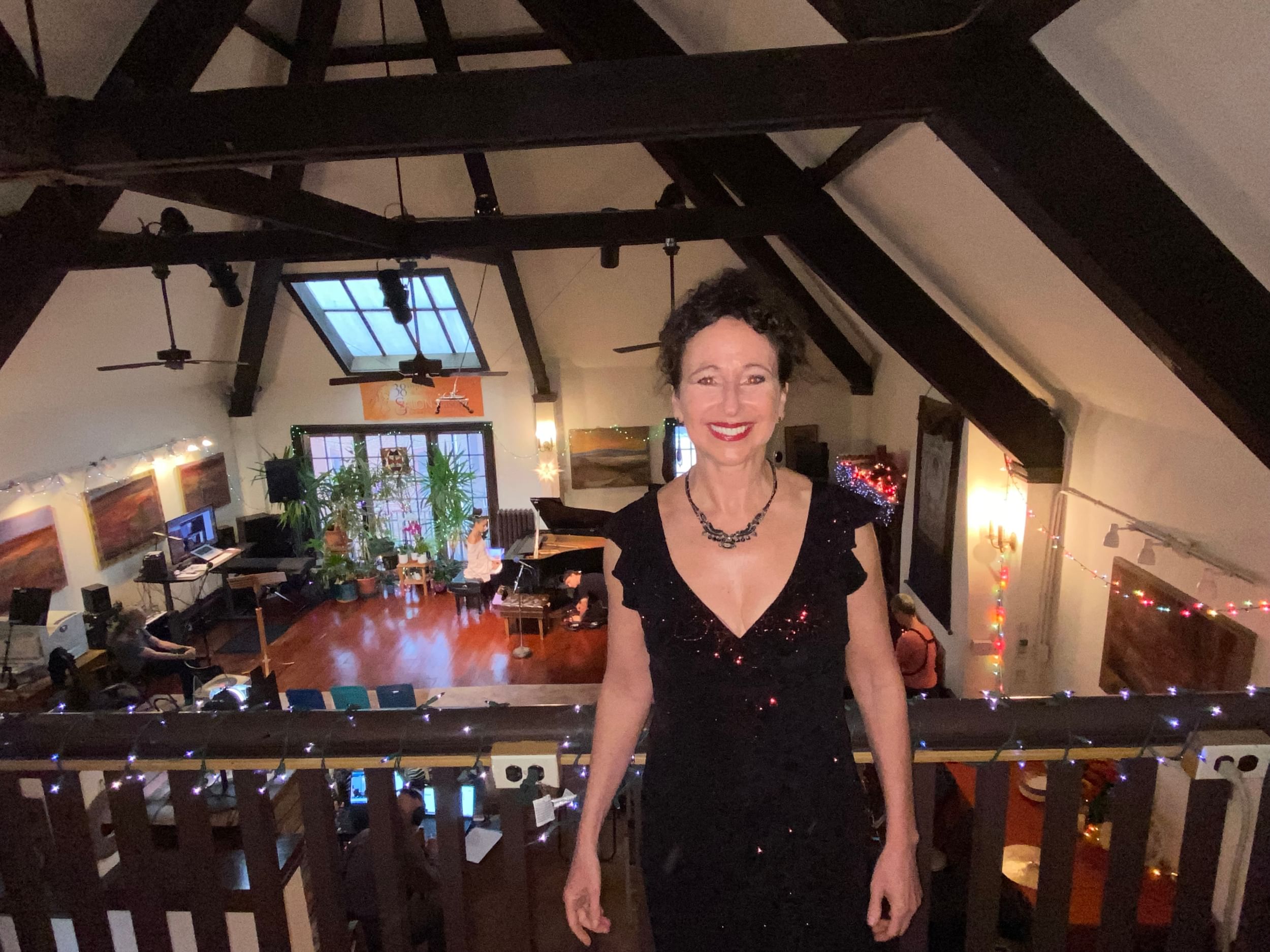 Clearfield, a white woman in a sparkly black dress, smiles in a spacious loft space outfitted for a concert behind her