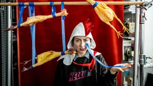 3 toy chickens taped to a wooden pole. A person wears a black shirt with letters, tape over half the word, leaving ‘hell’