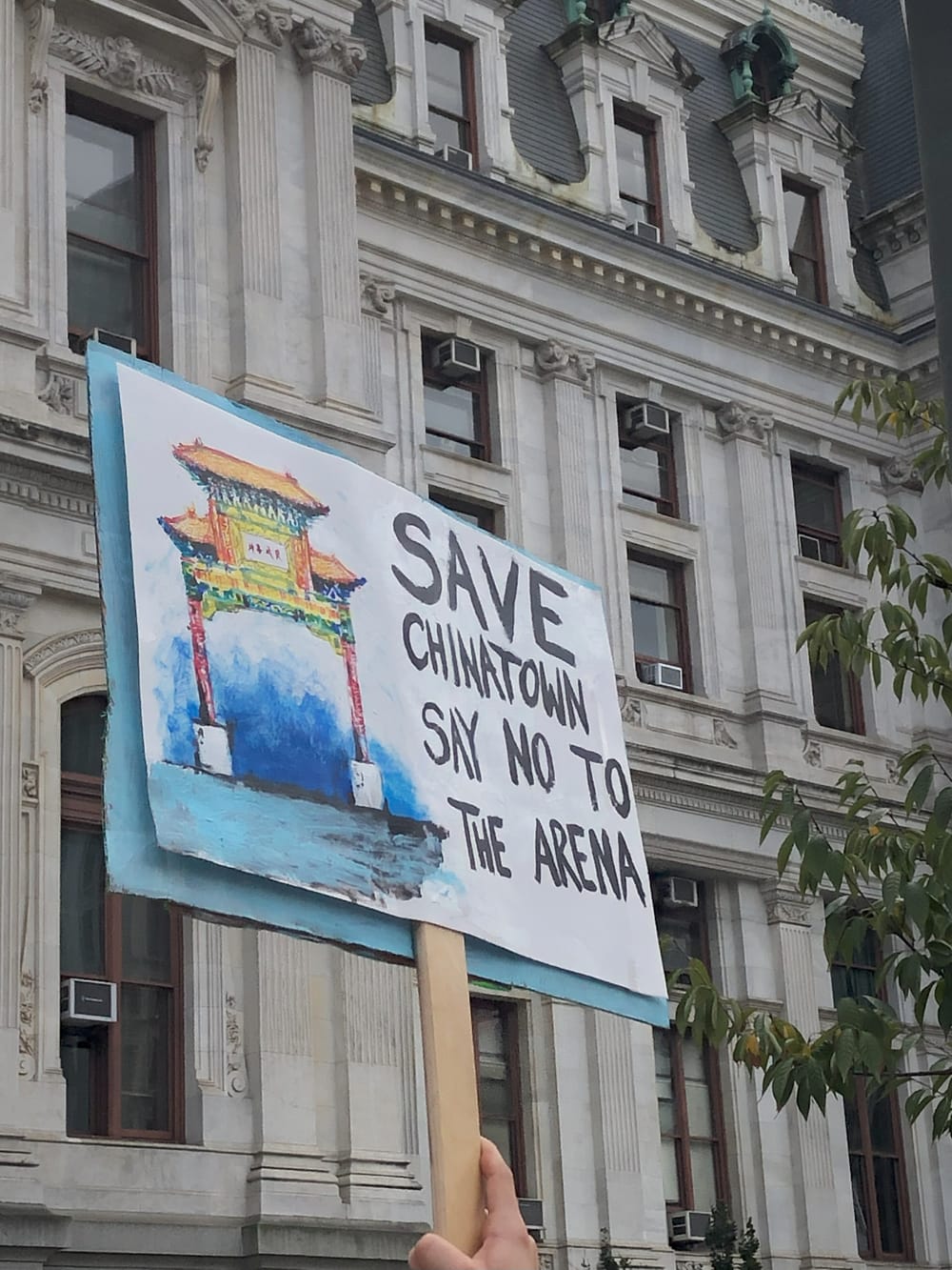 Handmade sign waving outside City Hall has painted illustration of Philly’s Chinatown arch and “say no the arena” on it