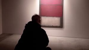 A shadowy, silhouetted image seen from behind a man regarding a red and white Rothko painting in a gallery.