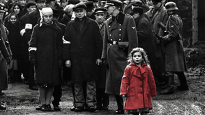 Film still. A young girl in red, everything else in black and white, in front of a crowd of Jewish people and Nazi soldiers