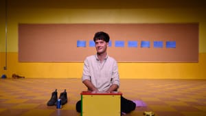 Cramer sits by a children's miniature piano in business casual, names on posted notes on the board behind them.