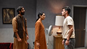 Ali & Zarif in brown Afghan clothes & Ayer in jeans and white tee face off tensely in a small living room with a red couch