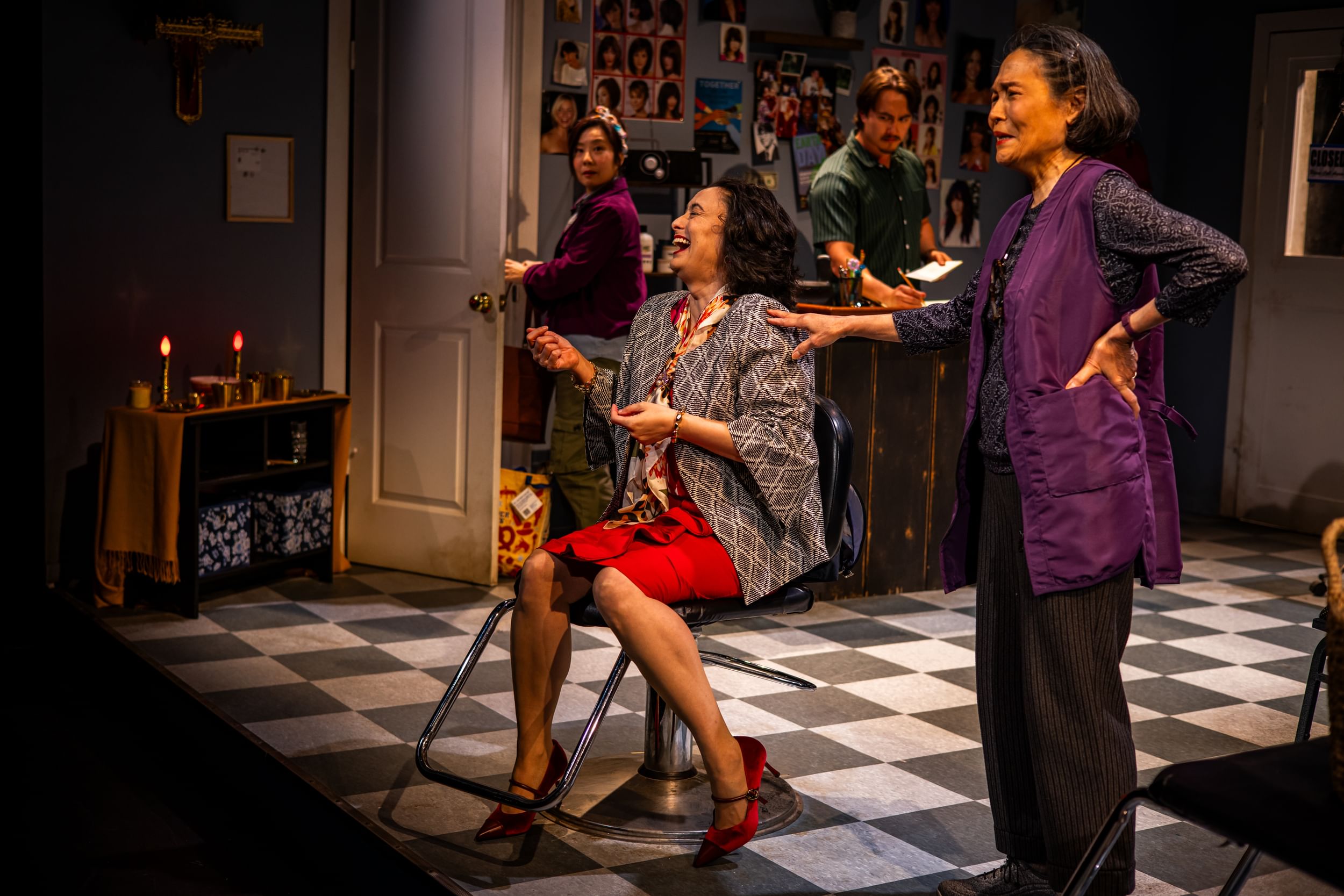 Liao, in red skirt & patterned jacket, laughs in a salon chair as the other actors on the salon set look worried.