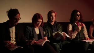 Photo of five people on a film panel in low light, holding microphones, with open scripts in their laps.