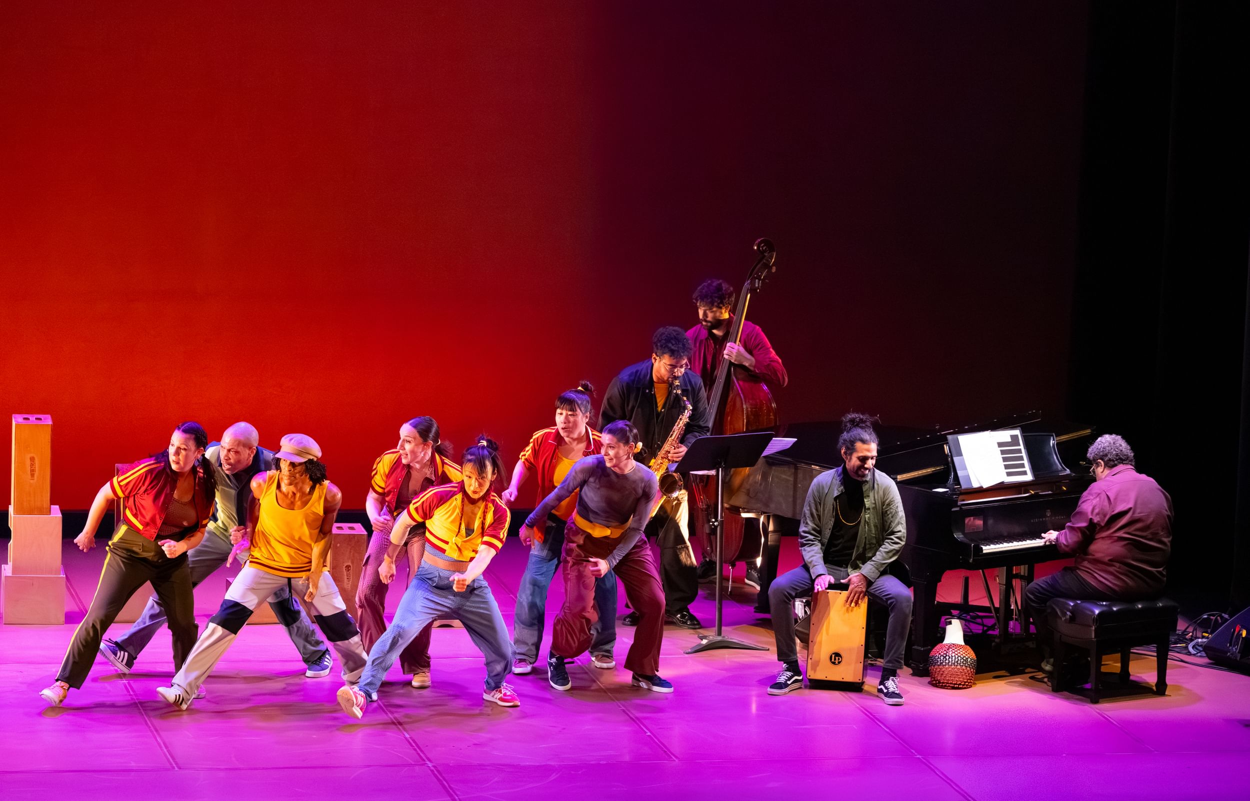 Seven dancers in casual clothes strike the same dynamic pose next to four musicians grouped at right.