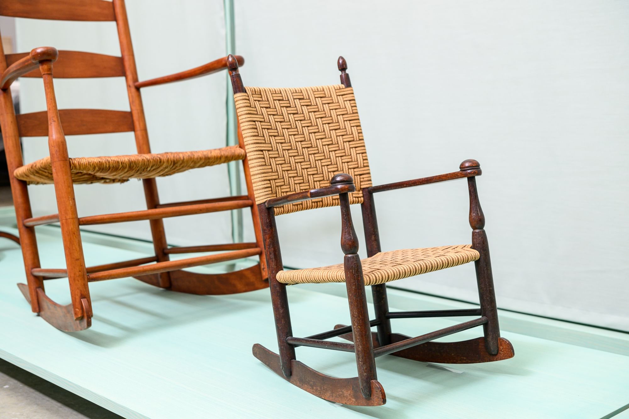 Closeup on two graceful and simple wooden rocking chairs from the 1800s, one adult and one child-sized.