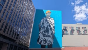 View of Sherald’s untitled six-story portrait mural of a Black teen in a yellow hat and striking black & white jacket.