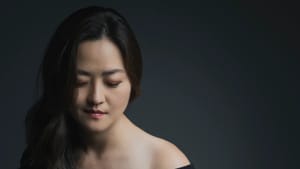 Cho, a Korean woman, looks down at her bandoneon, an accordion-like instrument. It’s extended out, falling over her lap