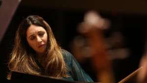 Close-up on Dinnerstein, a white woman in her early 50s with flowing brown hair, playing the piano among an orchestra.