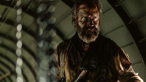 Tomilla, bearded, grimy, and bloody, wearing torn and filthy clothes, lurks angrily in some kind of tunnel.