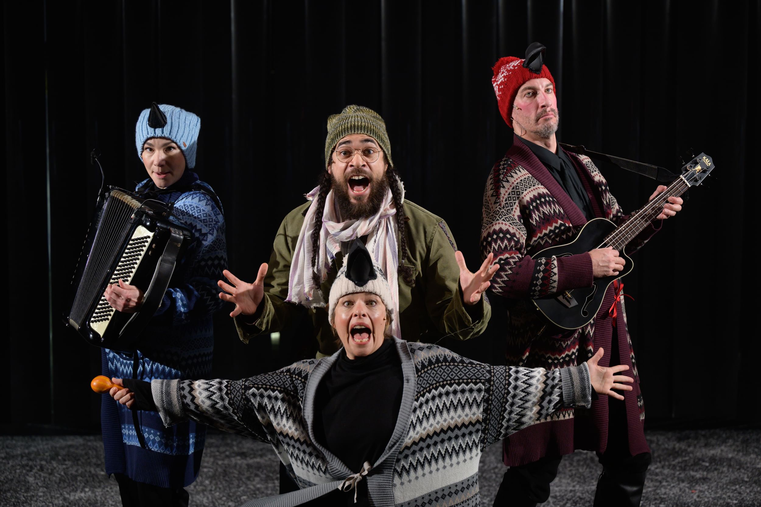 The actors, in cozy, Scandinavian-looking patterned sweaters and hats, pose together for a song, with an accordion & guitar