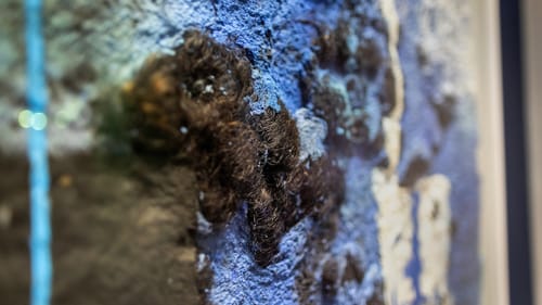 Close-up on Gbadebo’s work: textured daubs of blue and white material with dark-brown tufts of hair nestled in.