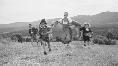 Black & white vintage outdoor photo of Martin in a dirndl running and laughing with the costumed kids over a hill.
